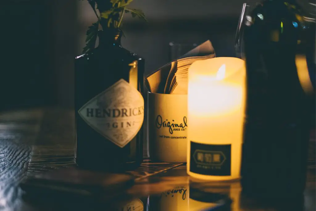 A beautiful bottle of Hendrick's Gin next to a candle on a wooden surface.