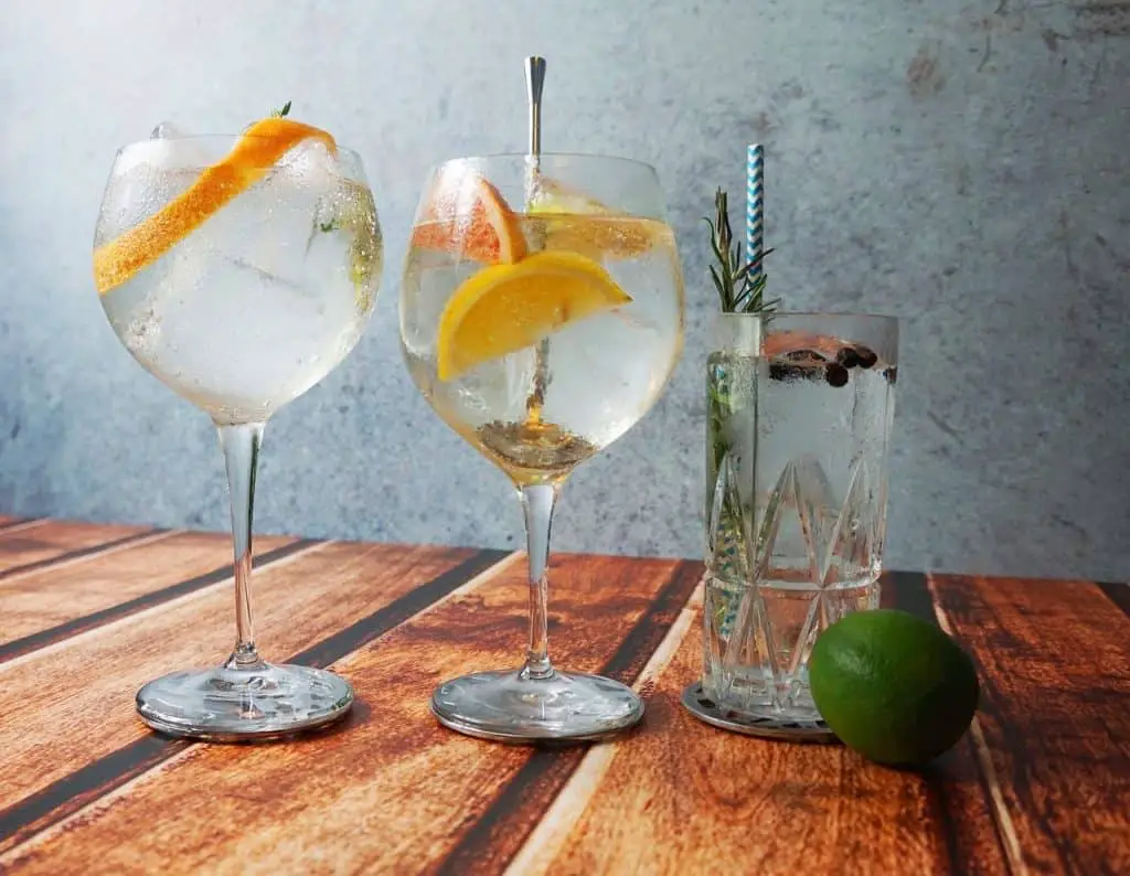 Three different gin cocktails in three different glasses with a lime on top of a wooden counter.