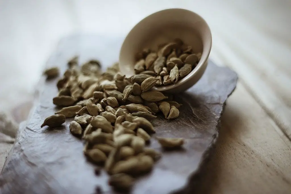 A bowl of cardamon pods was knocked over with cardamon spilling out over a stone slab.