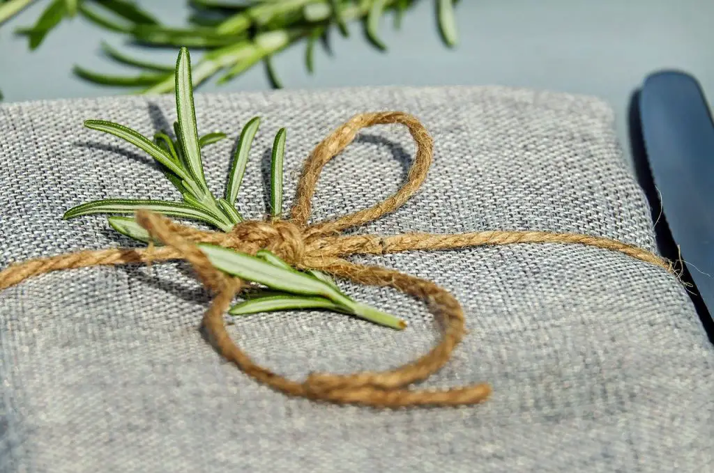 Beautiful sprigs of rosemary are displayed on a woven mat. The sprigs are secured with a brown rope.