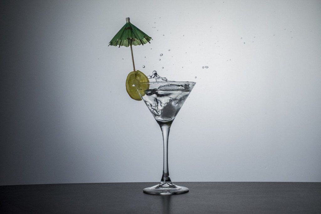 A cocktail glass filled with gin, a lemon wedge, and a green mini umbrella.