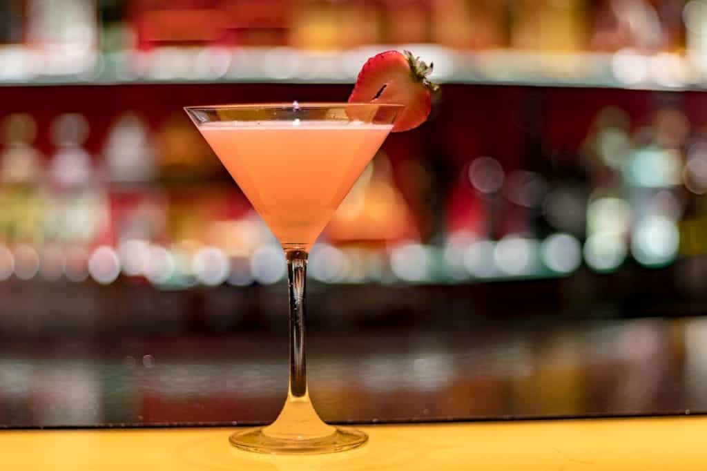 A beautiful looking cocktail, orange in color, with a strawberry on the edge of the glass.