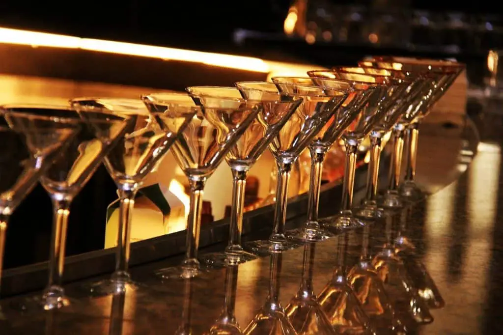 A number of cocktail glasses in a row on a bar.