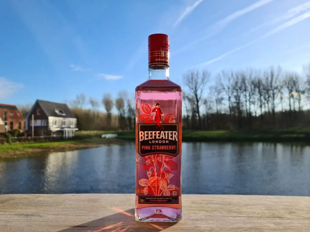 A bottle of Beefeater gin on a wooden table in front of a lake.