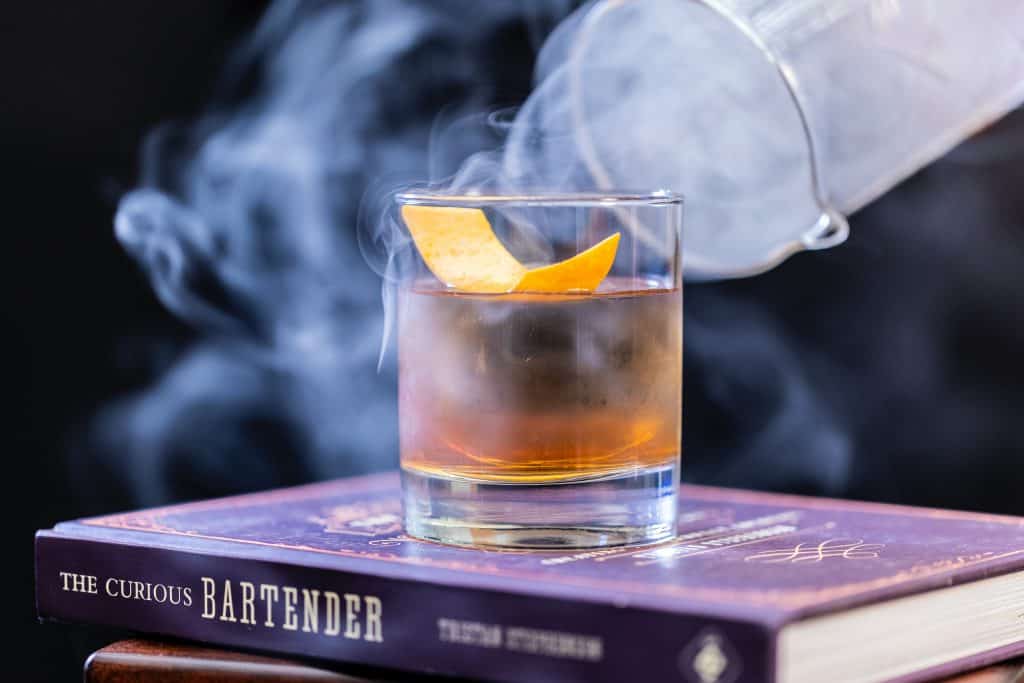 A gin cocktail in a short glass on top of a book titled: The Curious Bartender